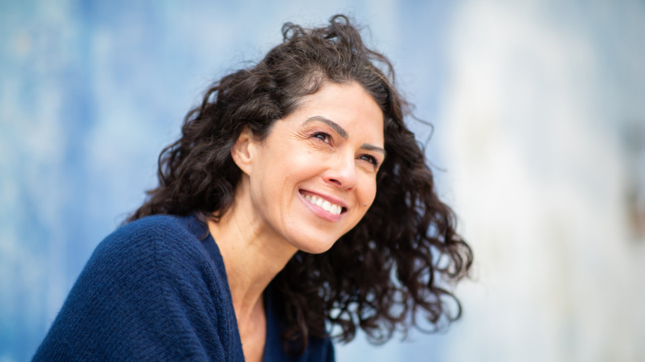 Smiling woman with curly hair looking off into the distance outdoors